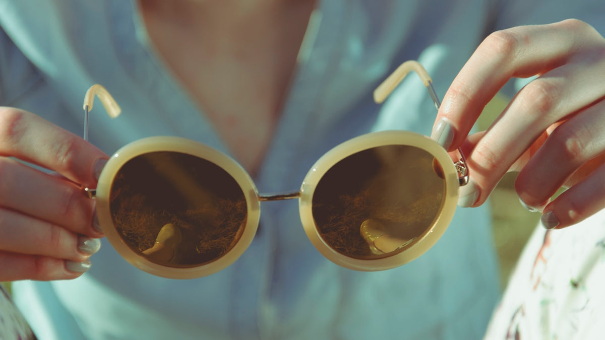 Woman holding a pair of round vintage-style sunglasses in daylight