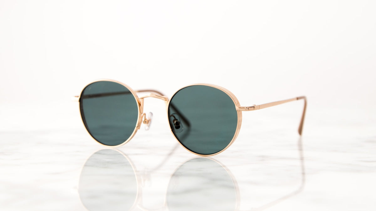 Gold-framed round vintage sunglasses on a white surface
