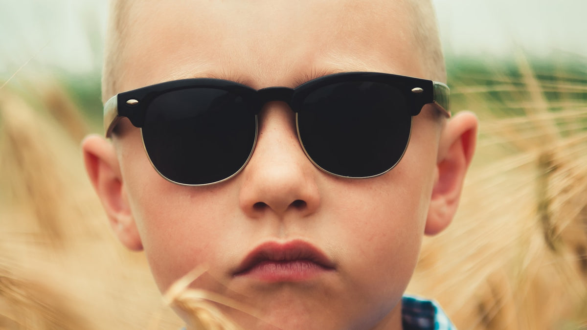 Young boy wearing black sunglasses outdoors on a sunny day