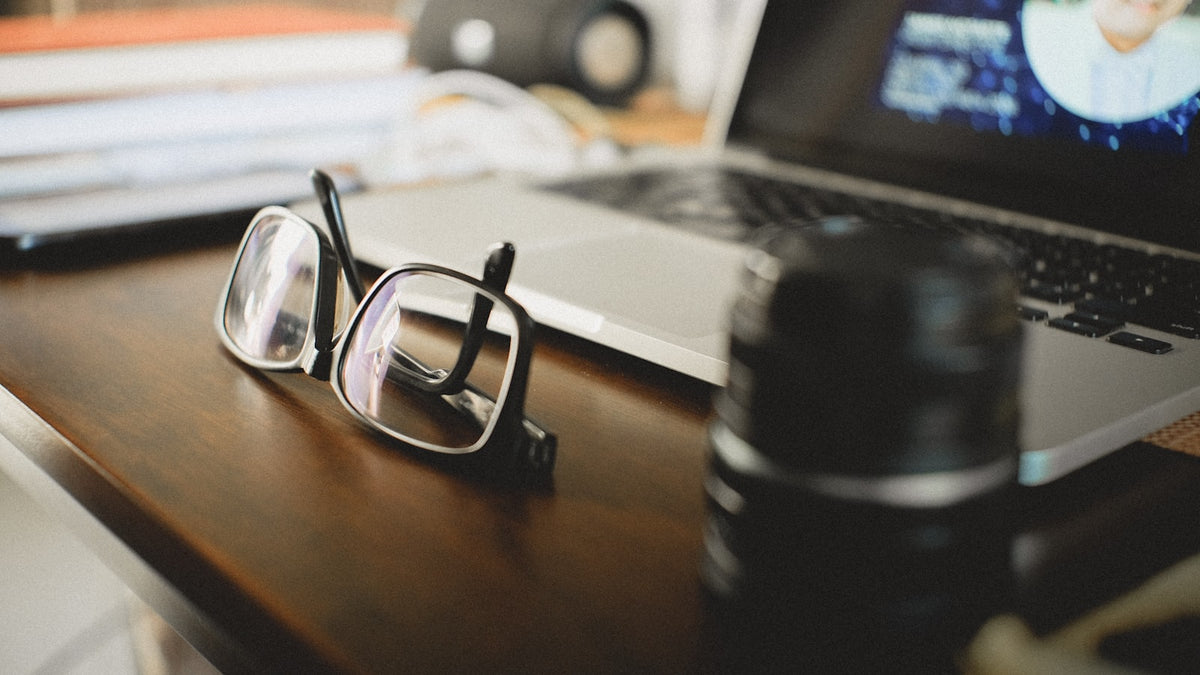 Eyeglasses on a wooden desk beside a laptop