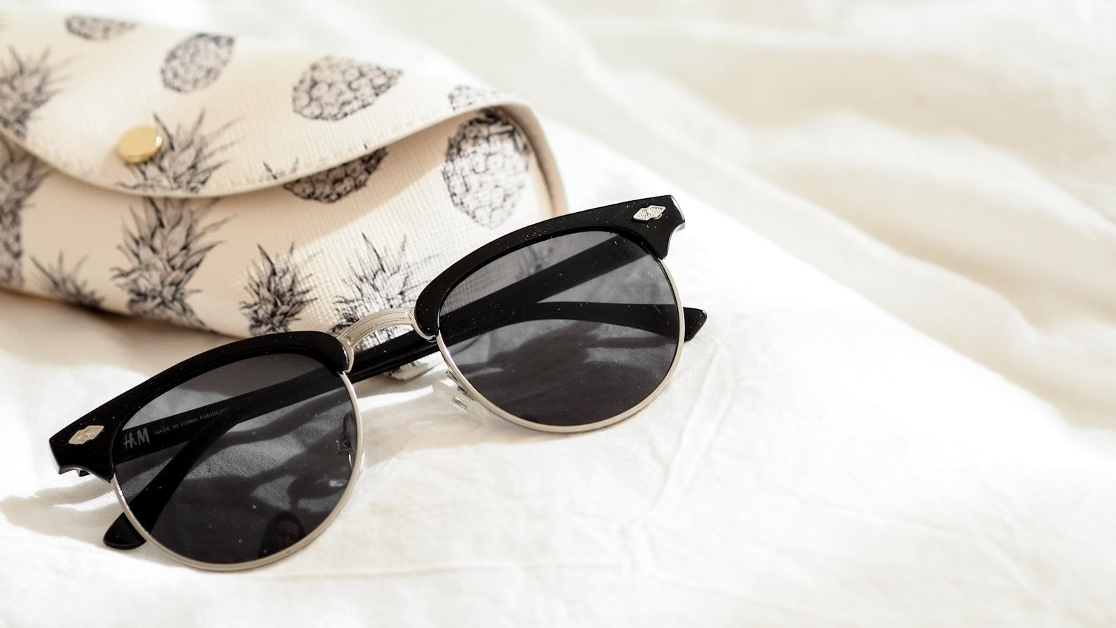 Black sunglasses beside a printed hard case on a bed — how to store sunglasses