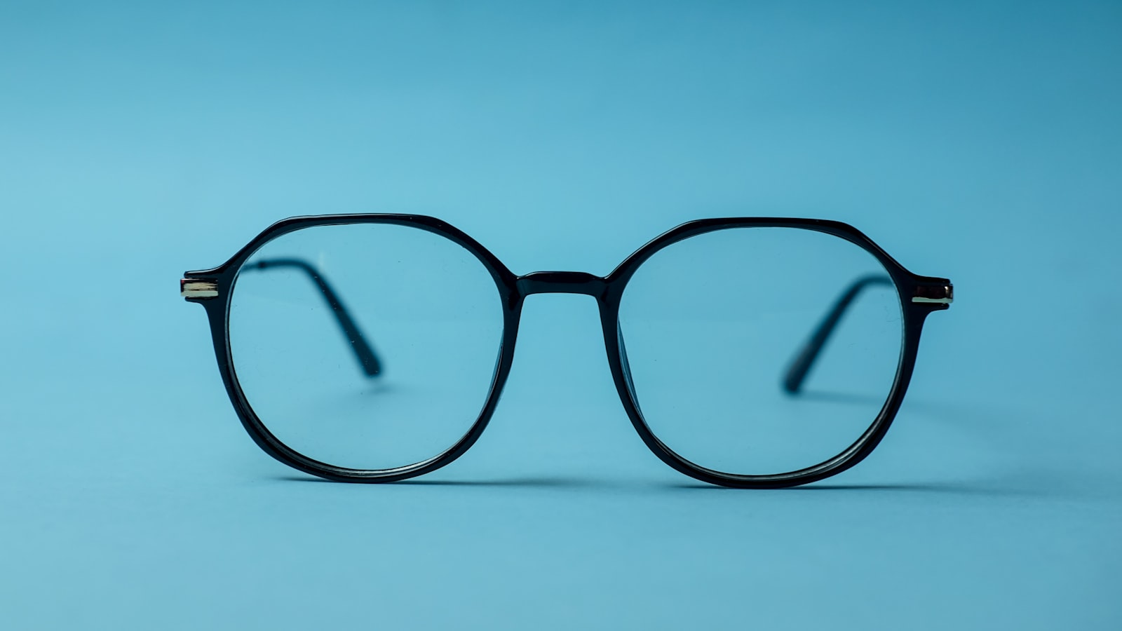 Geometric black eyeglasses centered on a plain blue background
