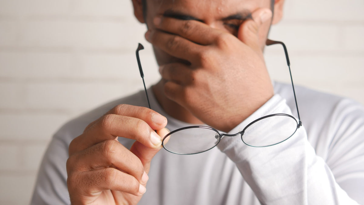 Man holding a pair of glasses up to his tired eyes