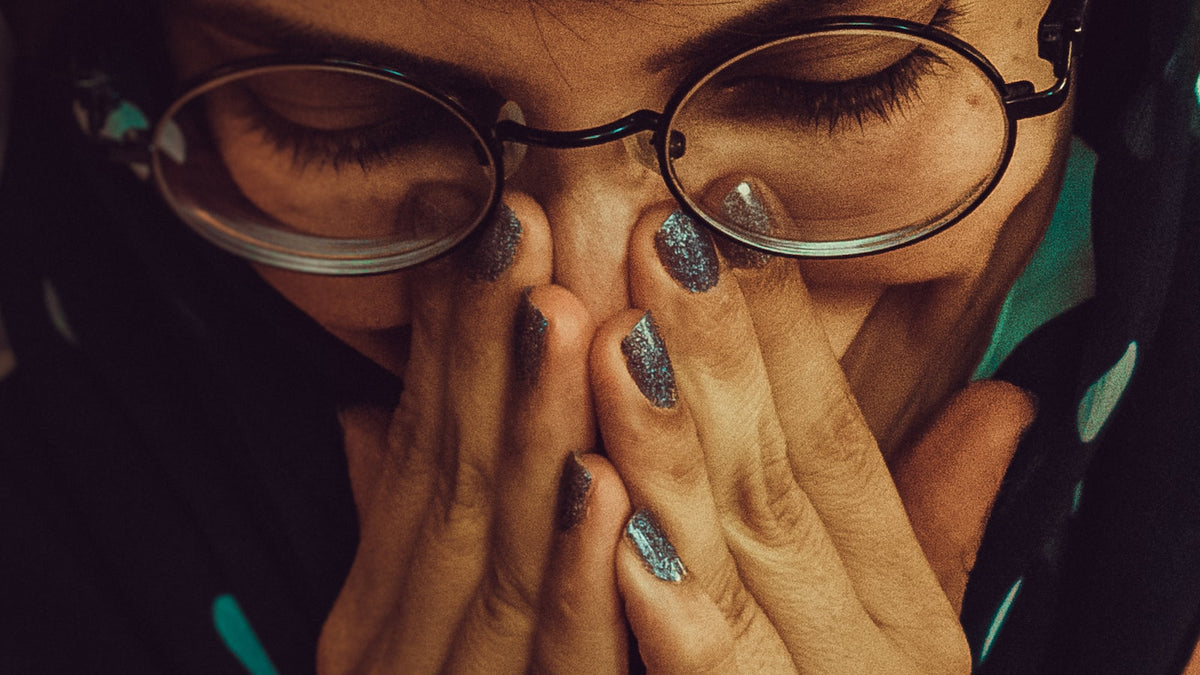 Person in glasses resting their head in their hands