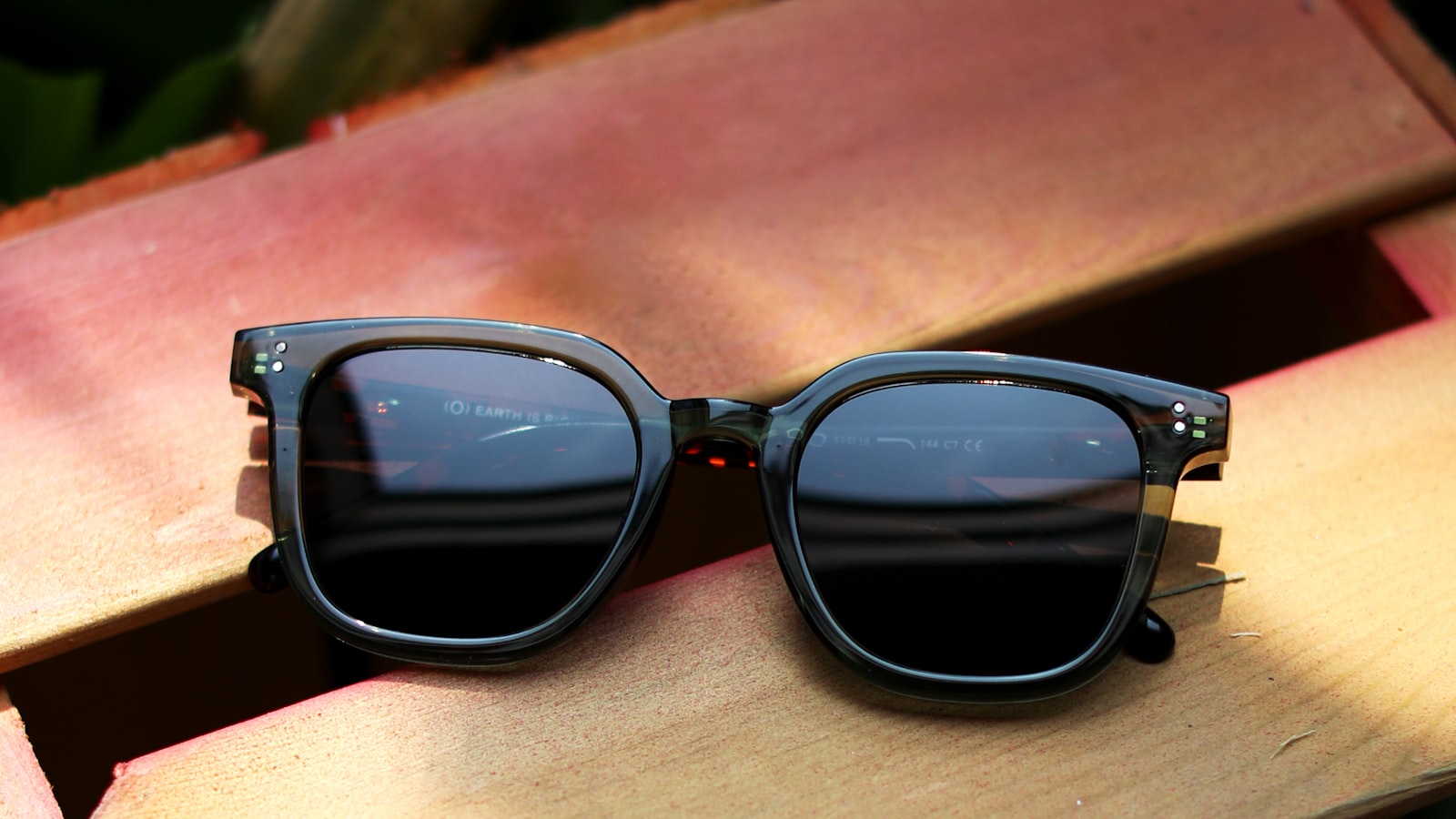 Chunky translucent acetate sunglasses resting on weathered painted wood