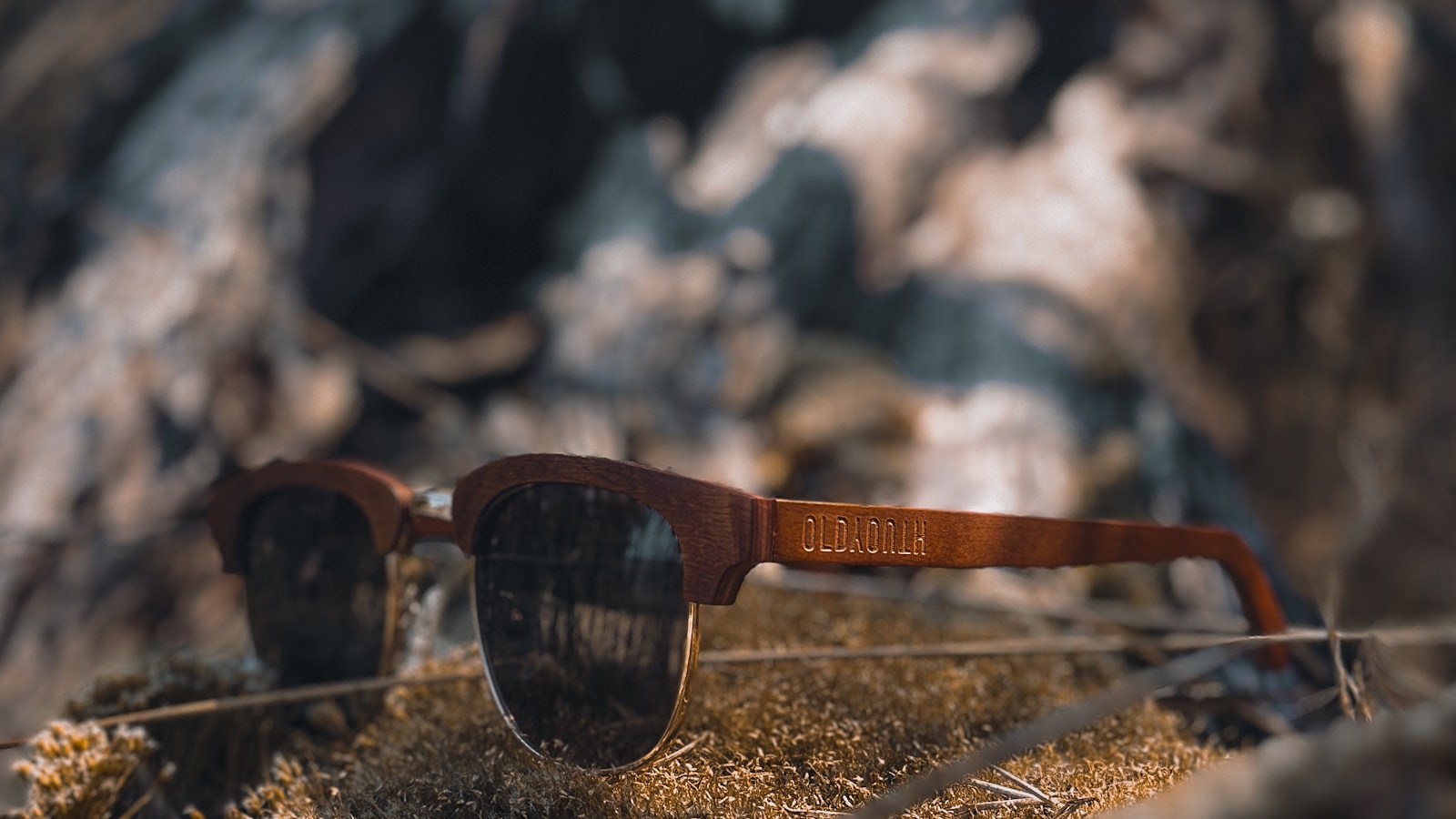 Wooden-framed sunglasses resting on sand in bright sunlight