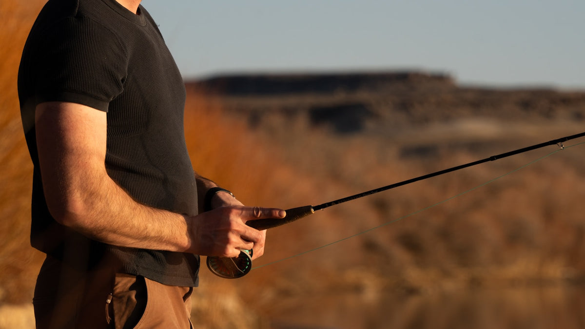 Angler on a beach holding a fishing pole in bright sun